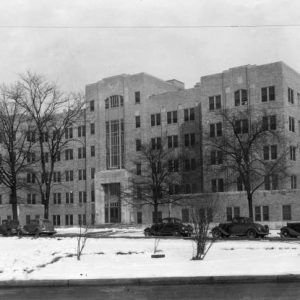 multistory brick building with bare trees on snow covered grounds and cars parked alongside