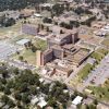 Campus of multistory buildings and outbuildings with parking lots and surrounding neighborhoods as seen from above