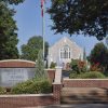 Multistory building with arched stained glass window and brick sign with flag pole in the foreground