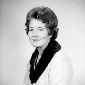 white woman seated smiling in fur lined coat and matching skirt