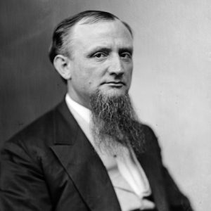 White man with beard sitting in suit and vest