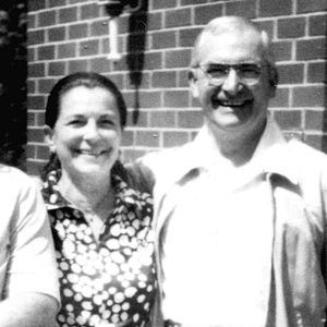 Smiling white woman in polka dot dress posing with white man in casual suit and glasses