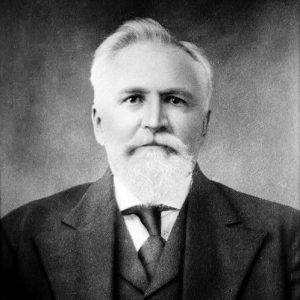 Portrait of an older white man with a white beard and receding hairline wearing a suit and tie