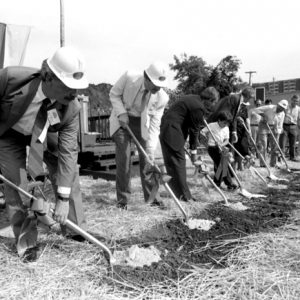 Groundbreaking ceremony including white men and child holding shovels with audience