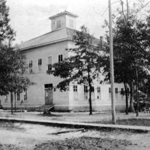 Boxy two story building with central tower with scattered trees around it