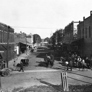 Busy street lined with brick buildings with pedestrians and horse-drawn carriages