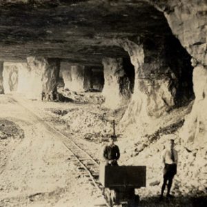 Interior expansive mine earth columns two white male figures foreground cart on tracks