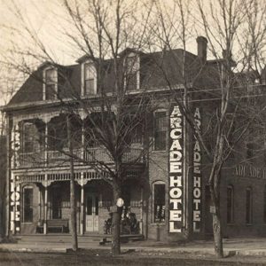 Two story brick building with balcony and vertical lettering "Arcade Hotel"