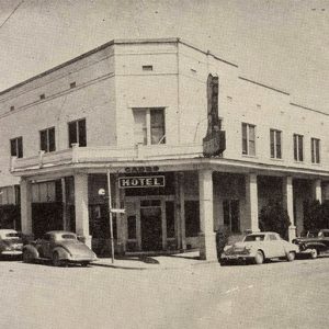 White multistory "Hotel" building with cars parked in front