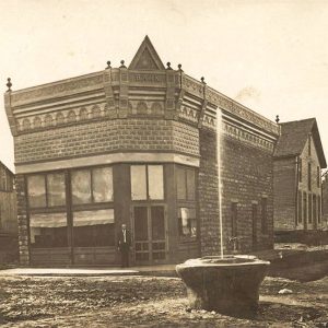 Brick corner building with ornate roof along road with water fountain in front