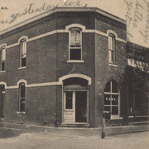 Postcard showing Two story brick building with corner entrance and arched windows; card has writing on it in pencil