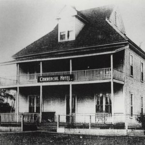 Multistory wooden building with balcony and a sign saying "Commercial Hotel"