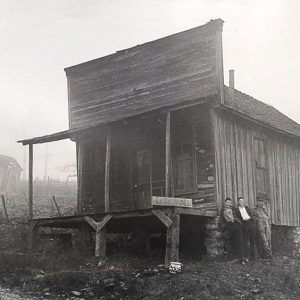 Wooden building with porch and three young men standing outside