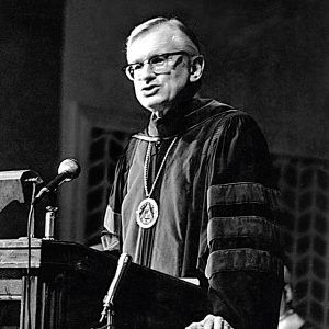 Man in graduation gown speaking at ;lectern