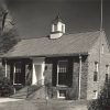 Single story brick building with cupola and water tower in the rear