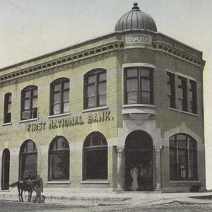 Two story building with dome over entrance and horse standing at sidewalk