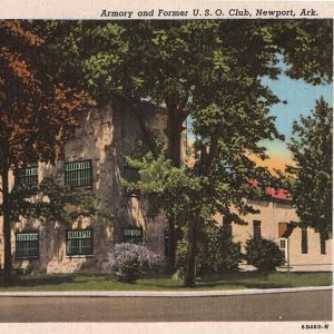 Multistory brick building with red roof behind trees