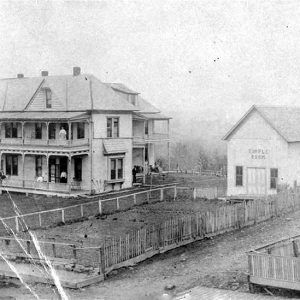 Large white wooden building with porch and balcony next to smaller white building