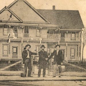 Three white men standing in front of multistory wooden house