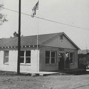 Single story building with two people and one car out front