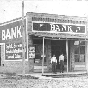 Two white men standing on porch of brick building with sign saying "Grant County Bank"