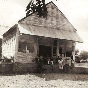 Group of men sitting on porch of wooden building with awning