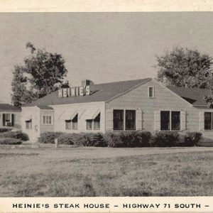 White single story building with siding and sign on roof saying "Heinie's"