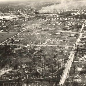 Aerial view of town with damaged buildings and smoke rising from certain places