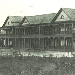 Long two story wooden building with wraparound balcony and porch