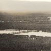 Aerial view of railroad bridge across flooded river with heavily forested land on both sides