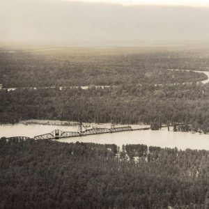 Aerial view of railroad bridge across flooded river with heavily forested land on both sides