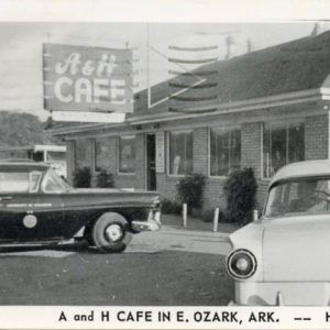 Single story white building with cars parked around it with sign saying "A and H Cafe"