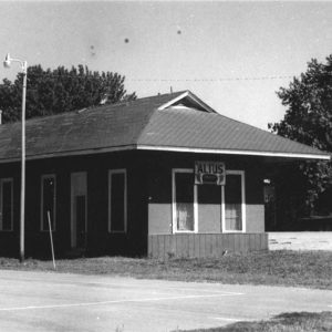 Small single story wooden building beside railroad tracks