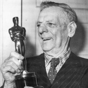 White man smiling in a polka dot tie holding statue