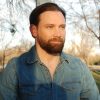 Bearded white man in denim shirt with snaps staring off into the distance