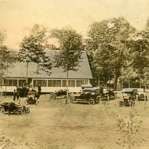 Large number of cars parked in front of building with trees all around