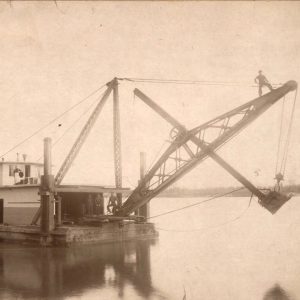 Men standing on boat equipped with large steam shovel