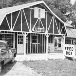 Barn-like building with pickup truck parked in front and sign saying "Feed Box"