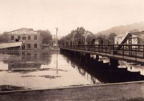 Bridge over river with multistory brick building in background by the far shore