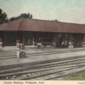 Low brick building next to railroad tracks with people sitting on benches.