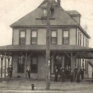 Multistory wooden building with people standing out front