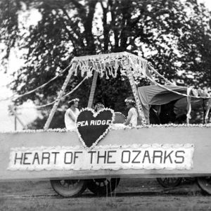 three white women on float decorated with flowers with "Pea Ridge Heart of the Ozarks" on the side