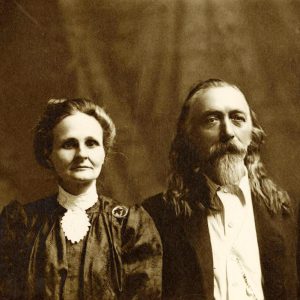 Older white man with long hair and beard beside woman with pulled-back hair in dress