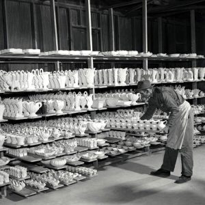 White man working at shelves filled with various types of pottery