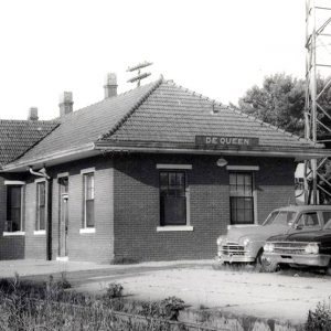 Single story brick building next to railroad tracks with cars parked at the end