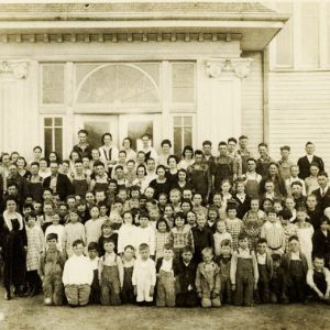 Large group of people in front of wooden building with arch window