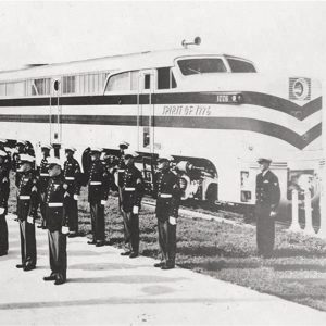 Large group of people in military garb standing in formation next to train