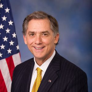 White man in suit and tie in front of American flag