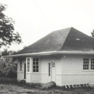 Single story white wooden building amid trees