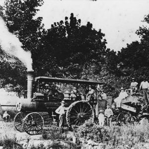 Men standing around tractor and farm implements with trees in the background